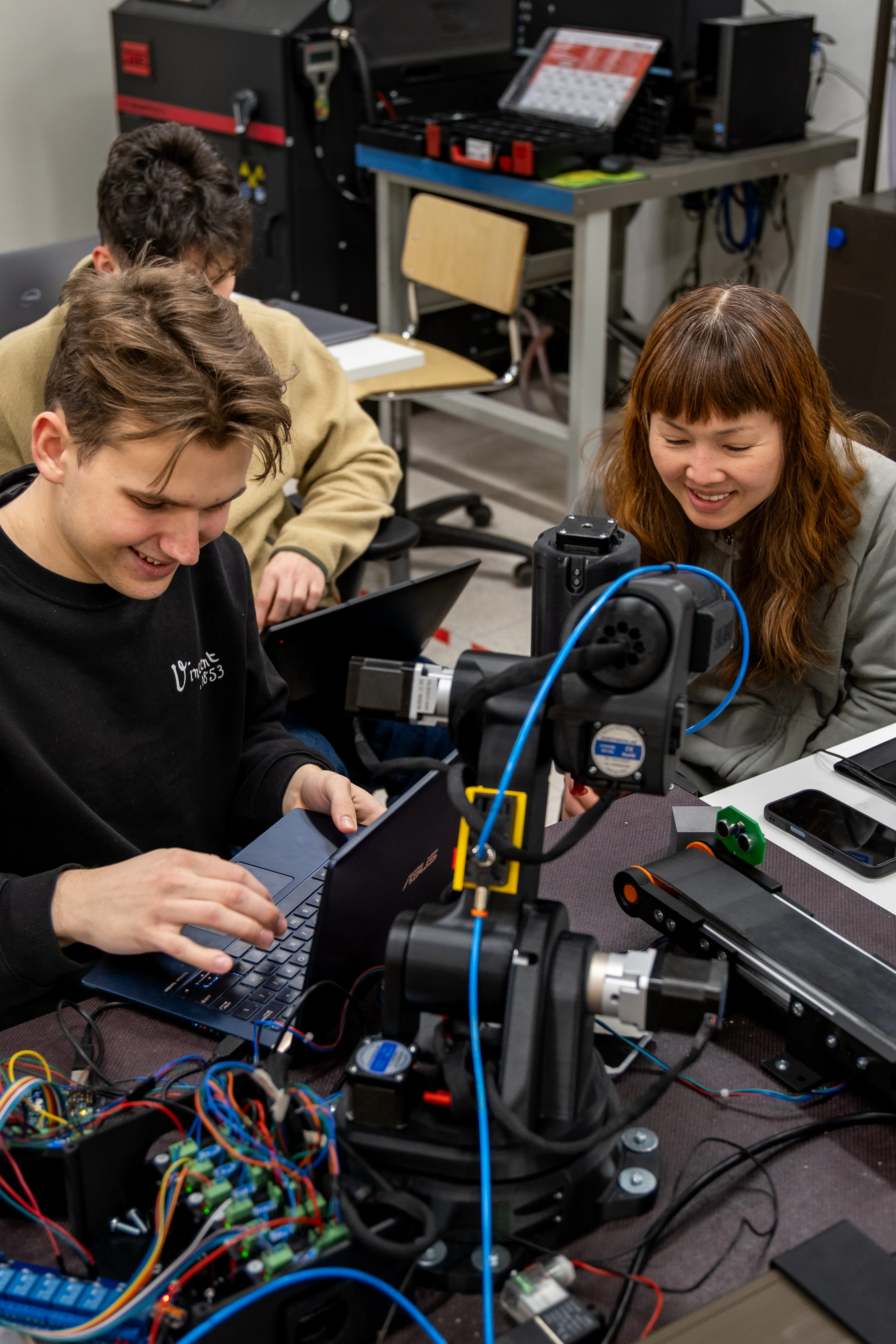 Two students programming Proto-GK-RA robot using a laptop.